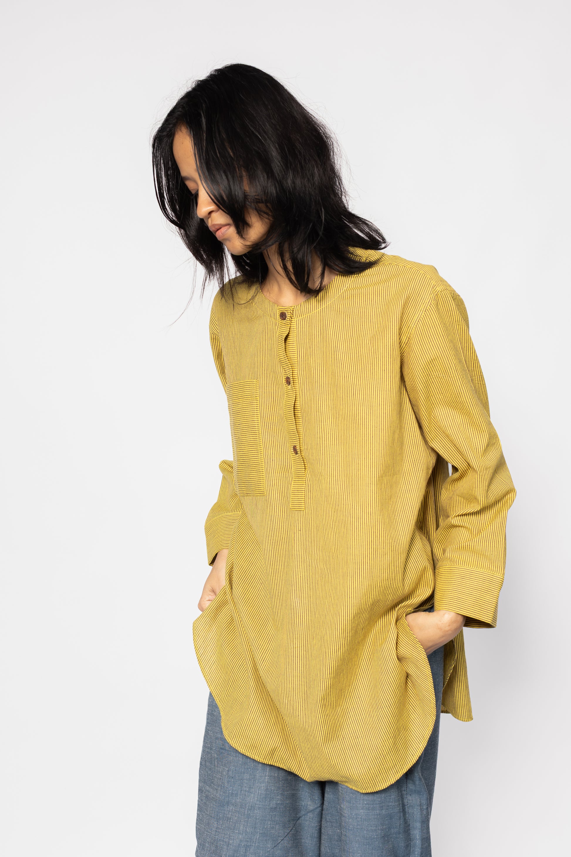 Plains Design - Harvest oversized shirt. Mustard yellow oversized shirt tunic with brown stripes featuring a rounded hem and side slits, wooden buttons, and front chest pocket. The tunic is made from handwoven cotton and has a relaxed fit with a patch pocket on one side.