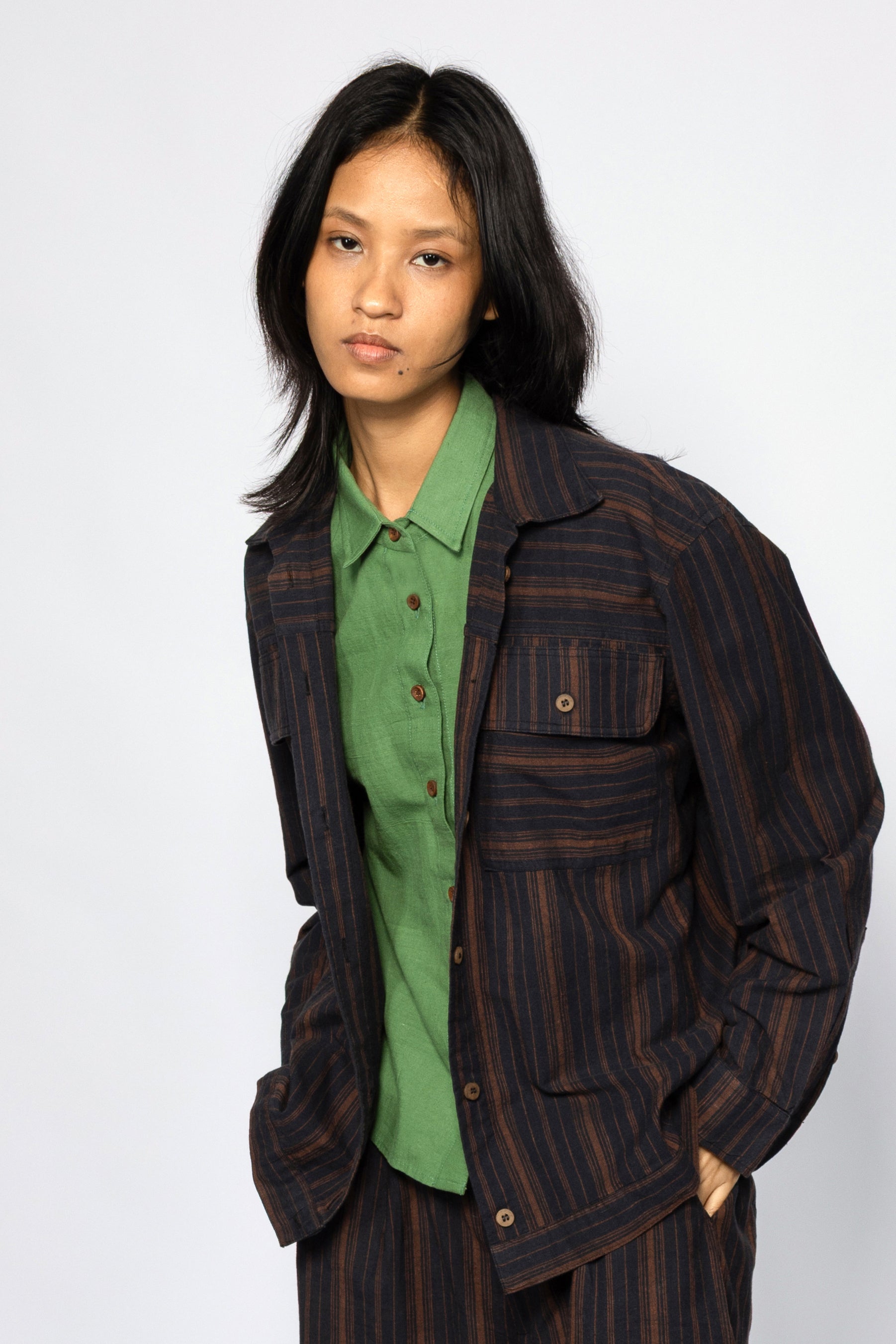 Plains Design - Brick Shirt. Oversized striped shirt in black and brick colours with long sleeves and square flap pockets on the chest. The shirt has contrasting stripes in a different direction on the pockets and sleeve hem. Paired with pants of the same handwoven cotton fabric.