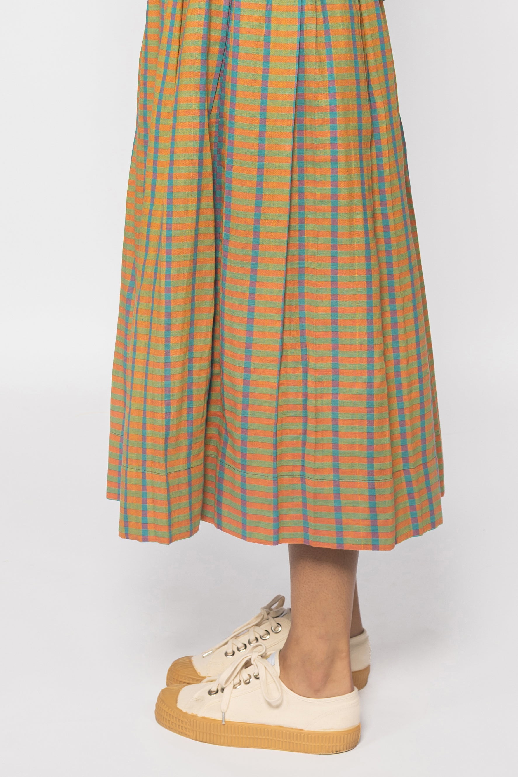 Plains Design - Twin skirt in Orange. Closeup bottom of a midi skirt in orange, blue and yellow checks with a relaxed fit. Paired with canvas shoes. Ethically handmade with handspun cotton in India.