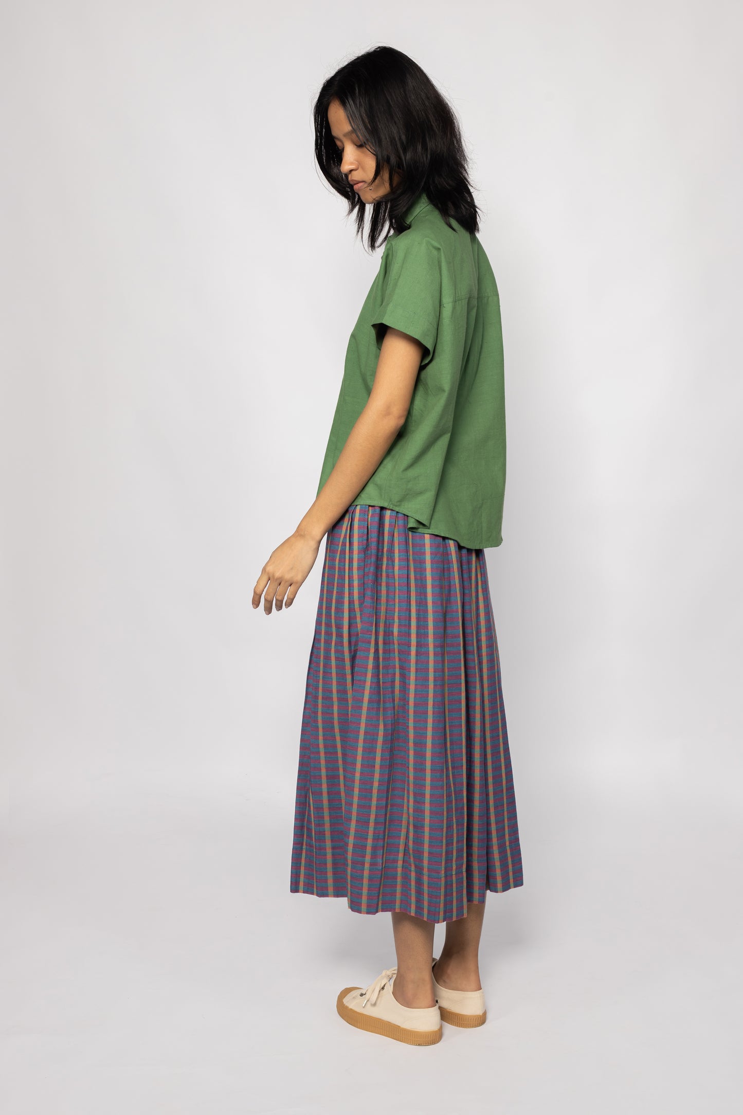 Plains Design - Twin Skirt in Purple. Side of view woman wearing purple striped skirt with pockets paired with a green shirt and canvas shoes. Handmade cotton. Ethical fashion.