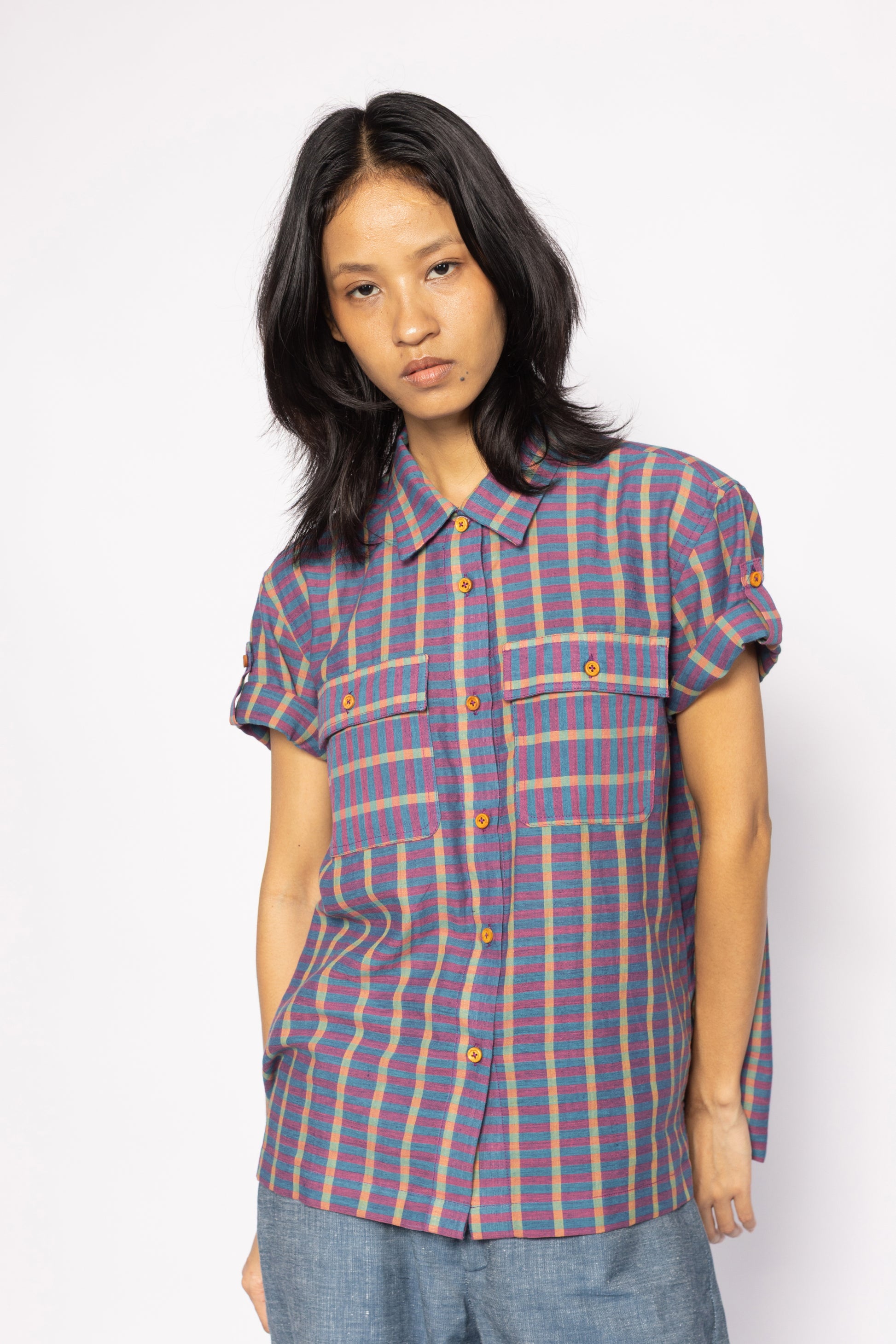 Plains Design - Twin Shirt in Purple. Striped purple and blue shirt with button-up front, short sleeves, chest pockets, and collar. Short foldable sleeves with buttons. Paired with blue denim pants. Handmade cotton. Sustainable fashion.