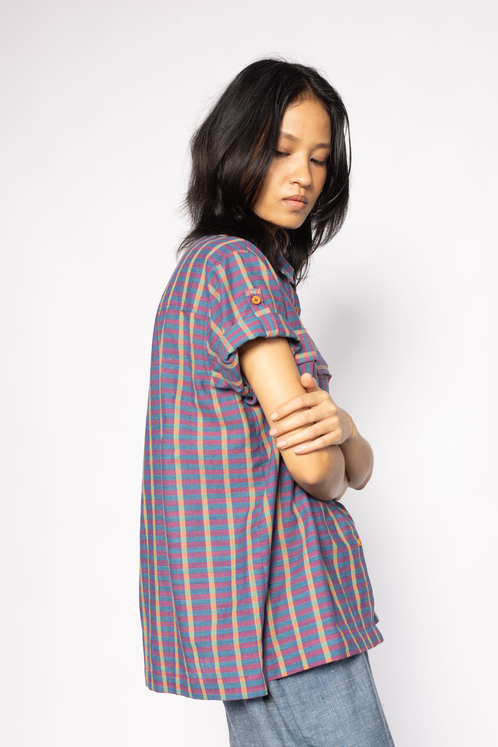Plains Design - Twin Shirt in Purple. Side view of model wearing striped purple and blue shirt with short folded sleeves and wooden buttons. Paired with blue denim pants. Handmade cotton. Ethical fashion.